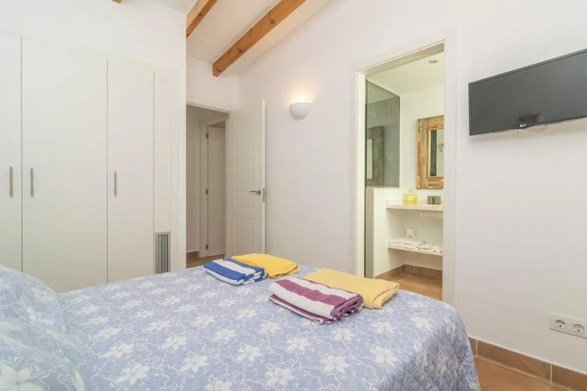 Un dormitorio con una cama estampada, toallas dobladas y un televisor en la pared.