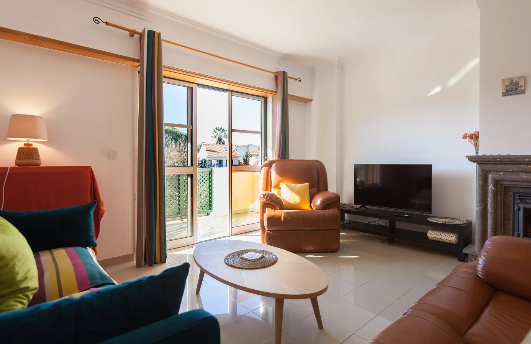 Sala de estar con asientos, una mesa de centro y un televisor junto a una puerta al balcón.