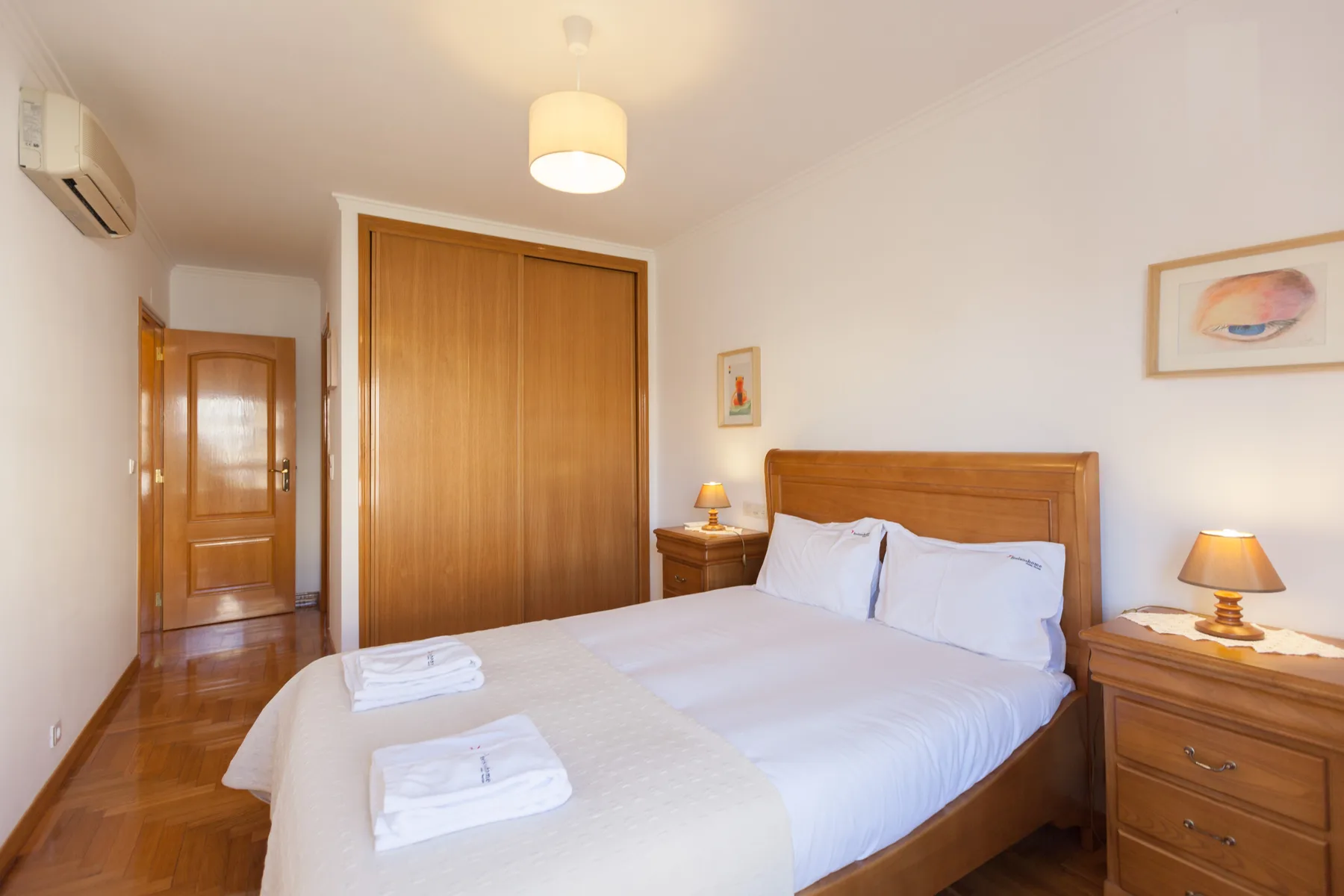 Dormitorio con una cama bien arreglada, un armario de madera y mesillas de noche.