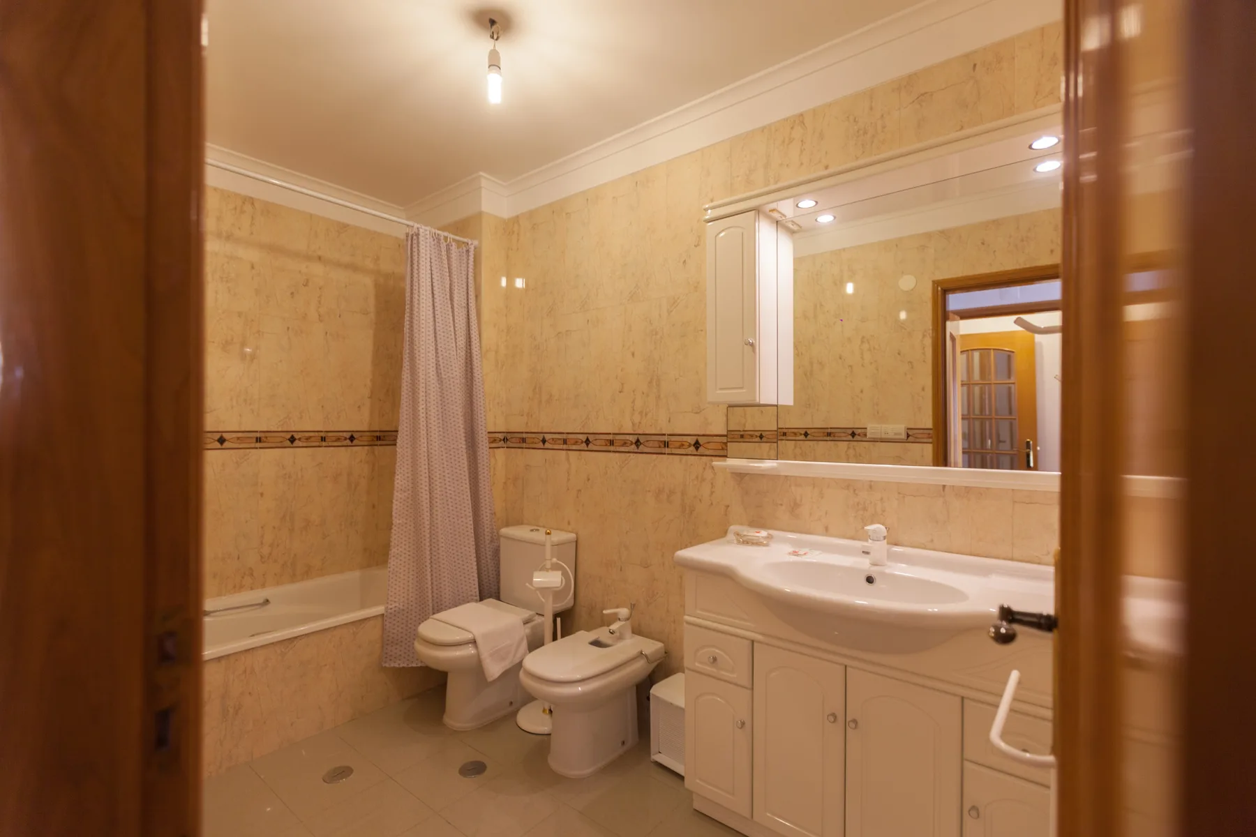 Un baño con bañera, inodoro y lavabo bajo un espejo grande.