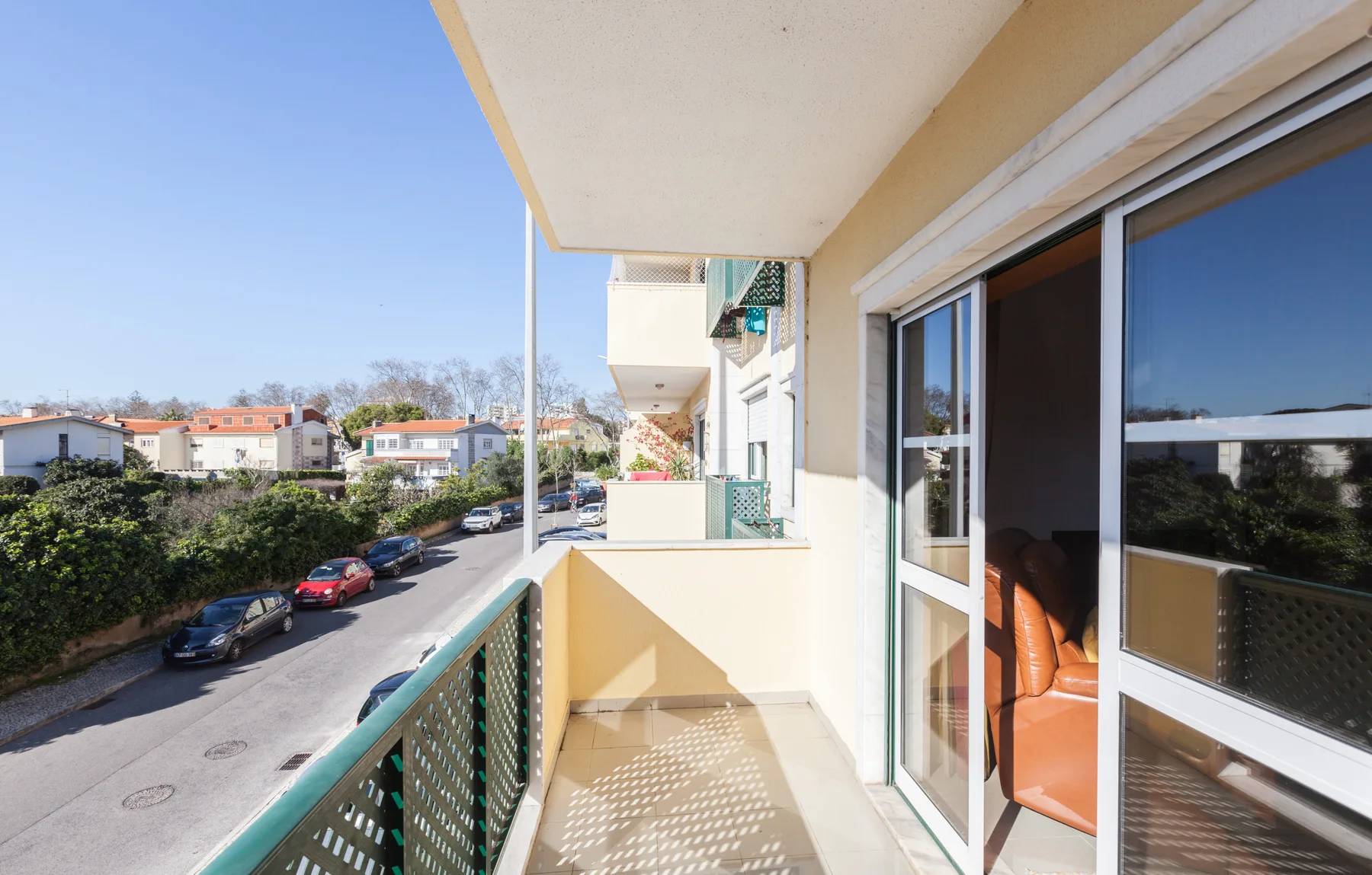 Un balcón da a una calle residencial, con puertas corredizas de vidrio hacia el interior.