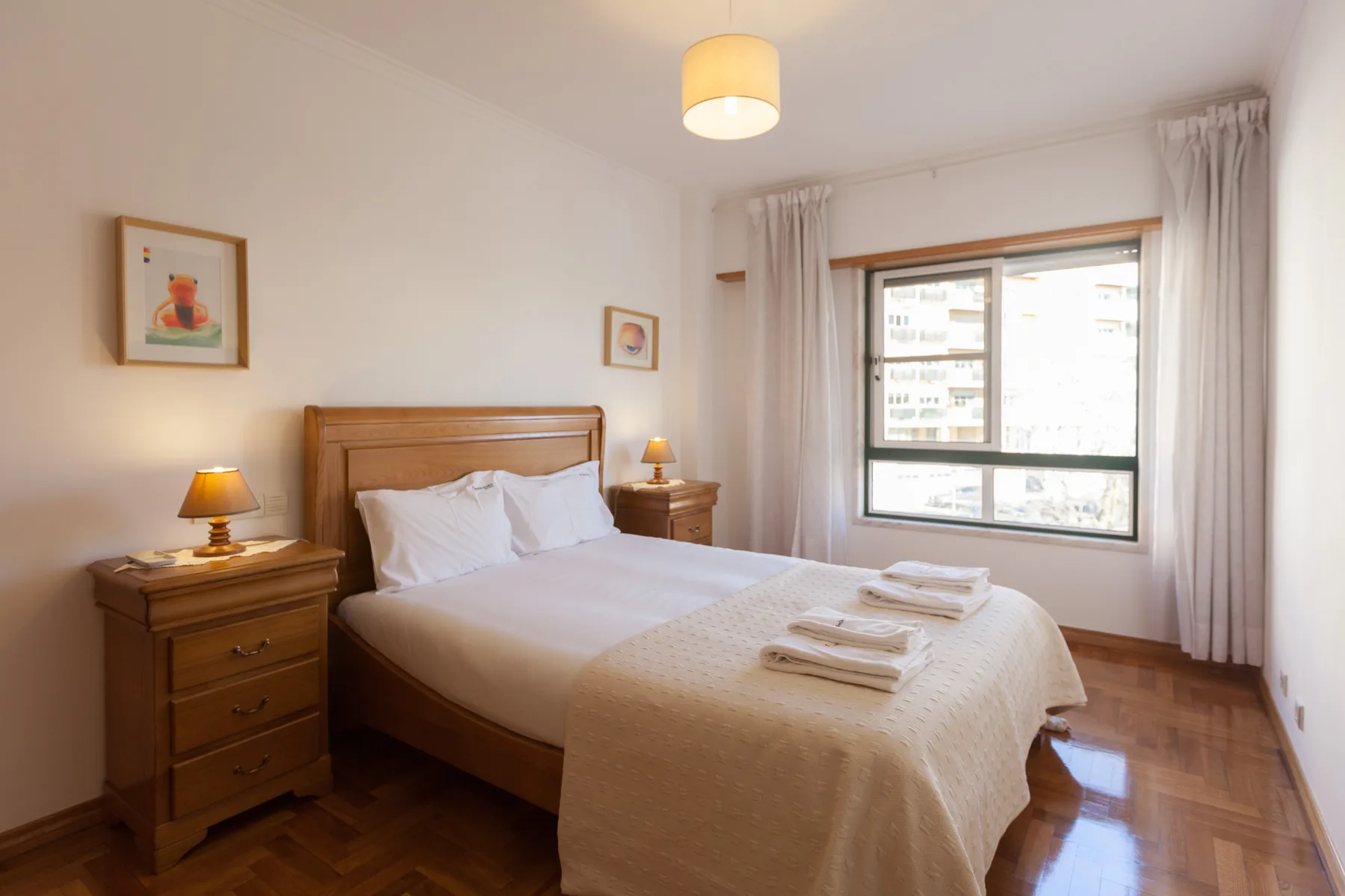 Un dormitorio luminoso con cama doble, mesitas de noche y una ventana grande.