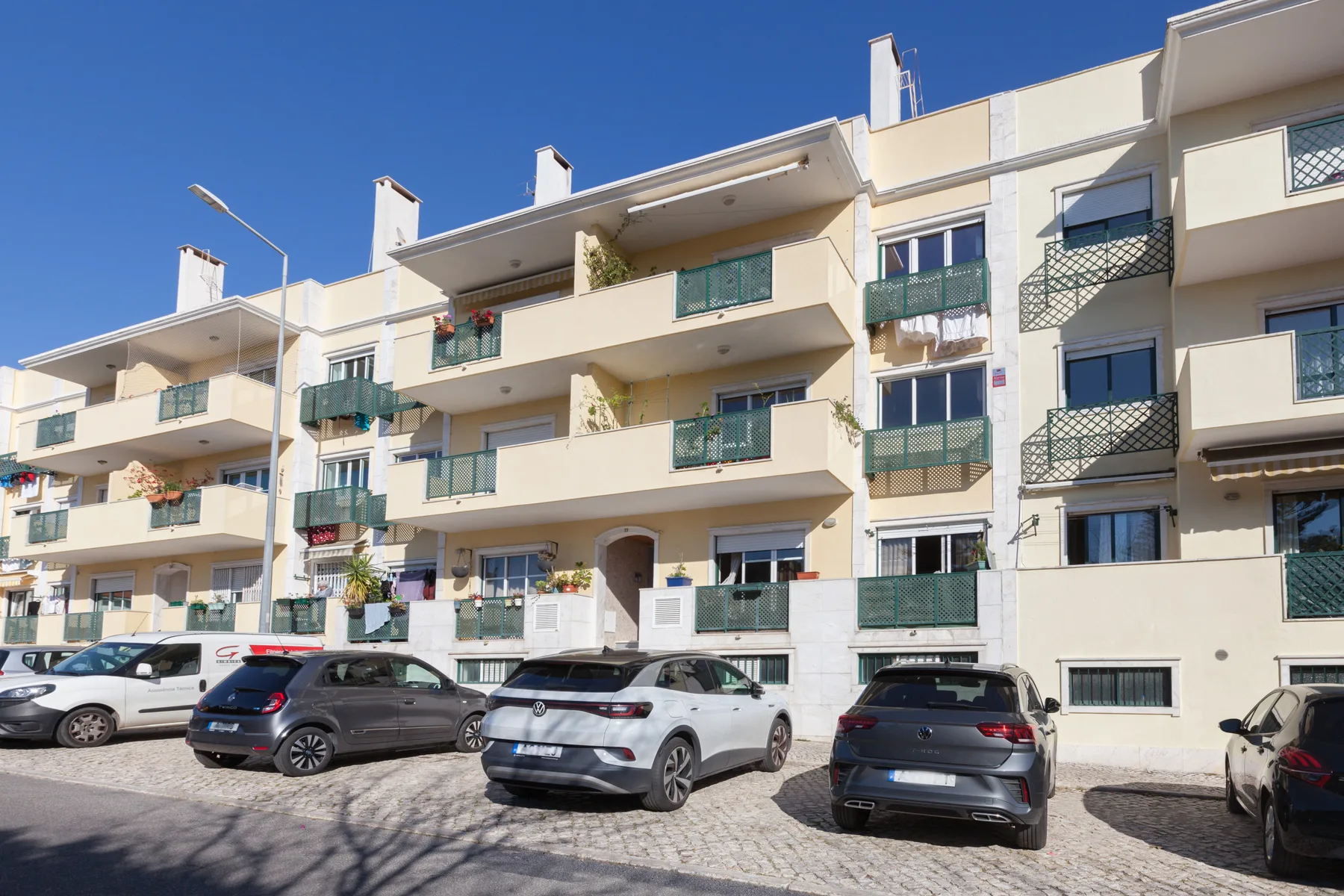Edificio de apartamentos con balcones y coches estacionados en la calle.
