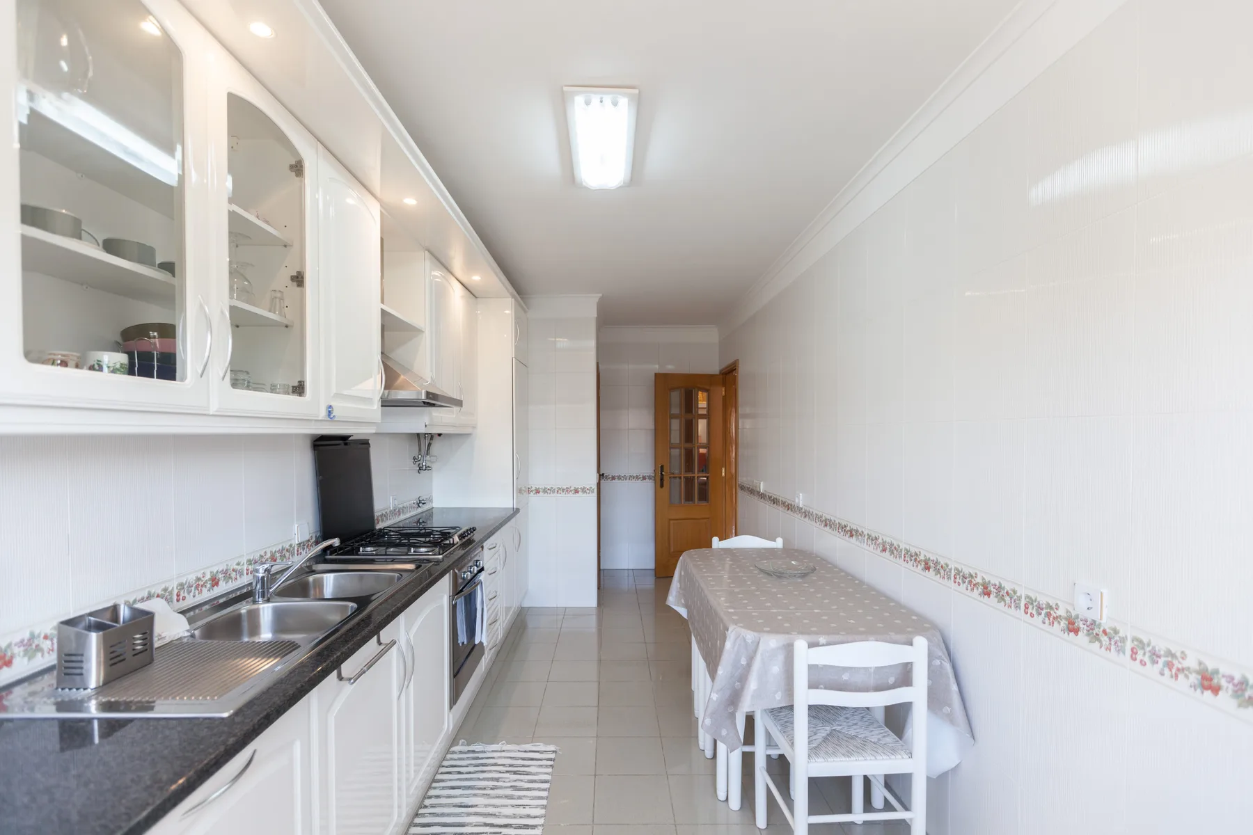 Una cocina estrecha con armarios blancos, una encimera y una mesa de comedor.