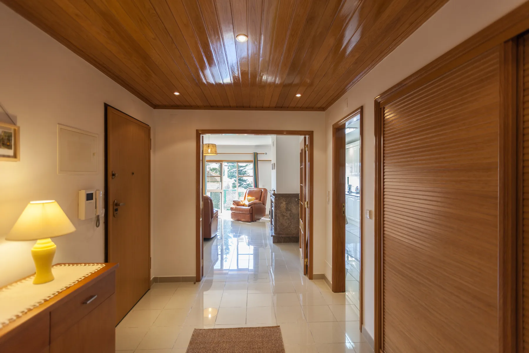 Un pasillo de apartamento con techo de madera y una sala visible a través de la puerta.