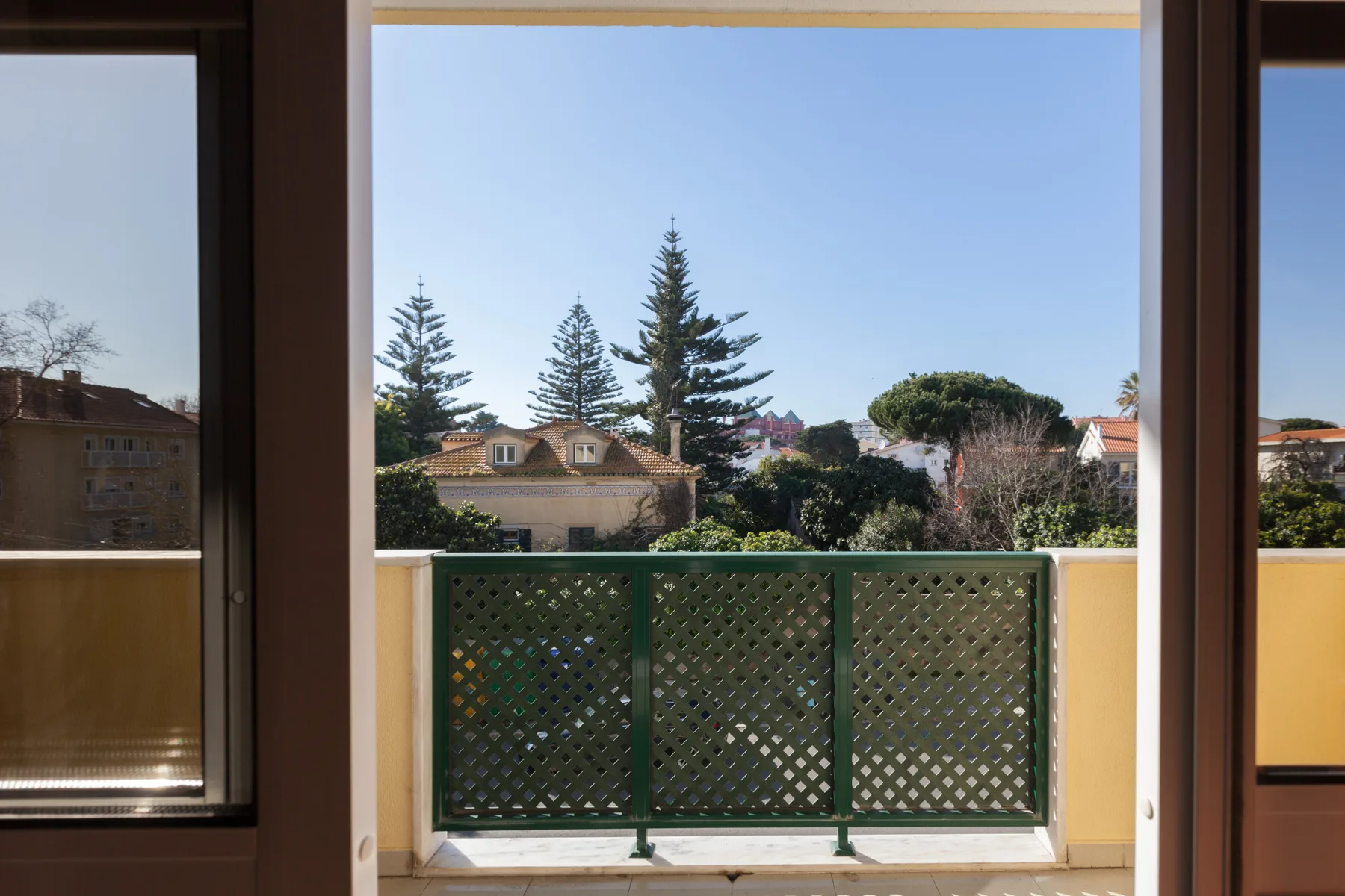 Un balcón se abre a vistas de casas vecinas, árboles y cielo despejado.