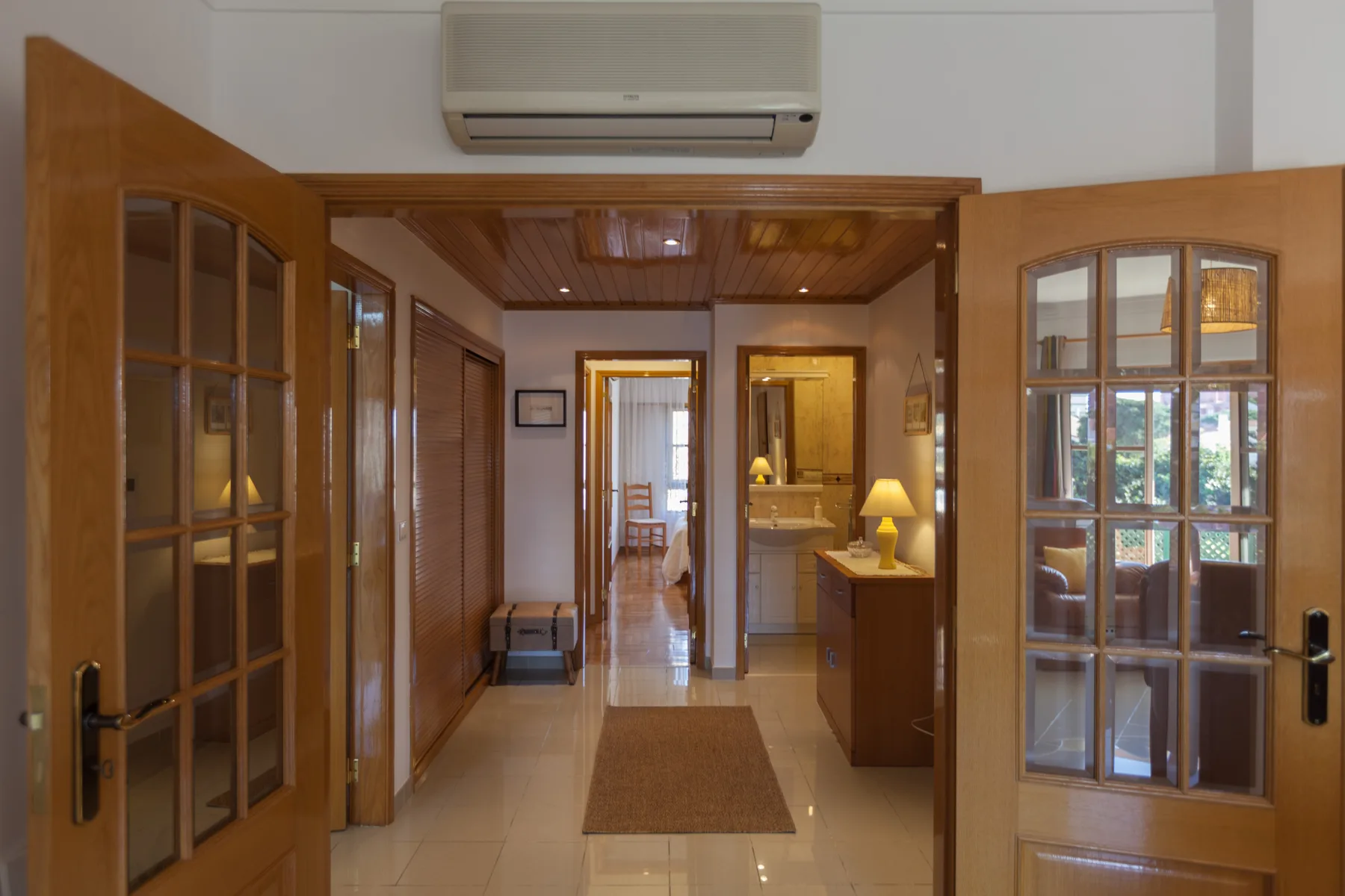 Un pasillo con puertas de madera abiertas conduce hacia una pequeña zona con lavabo.