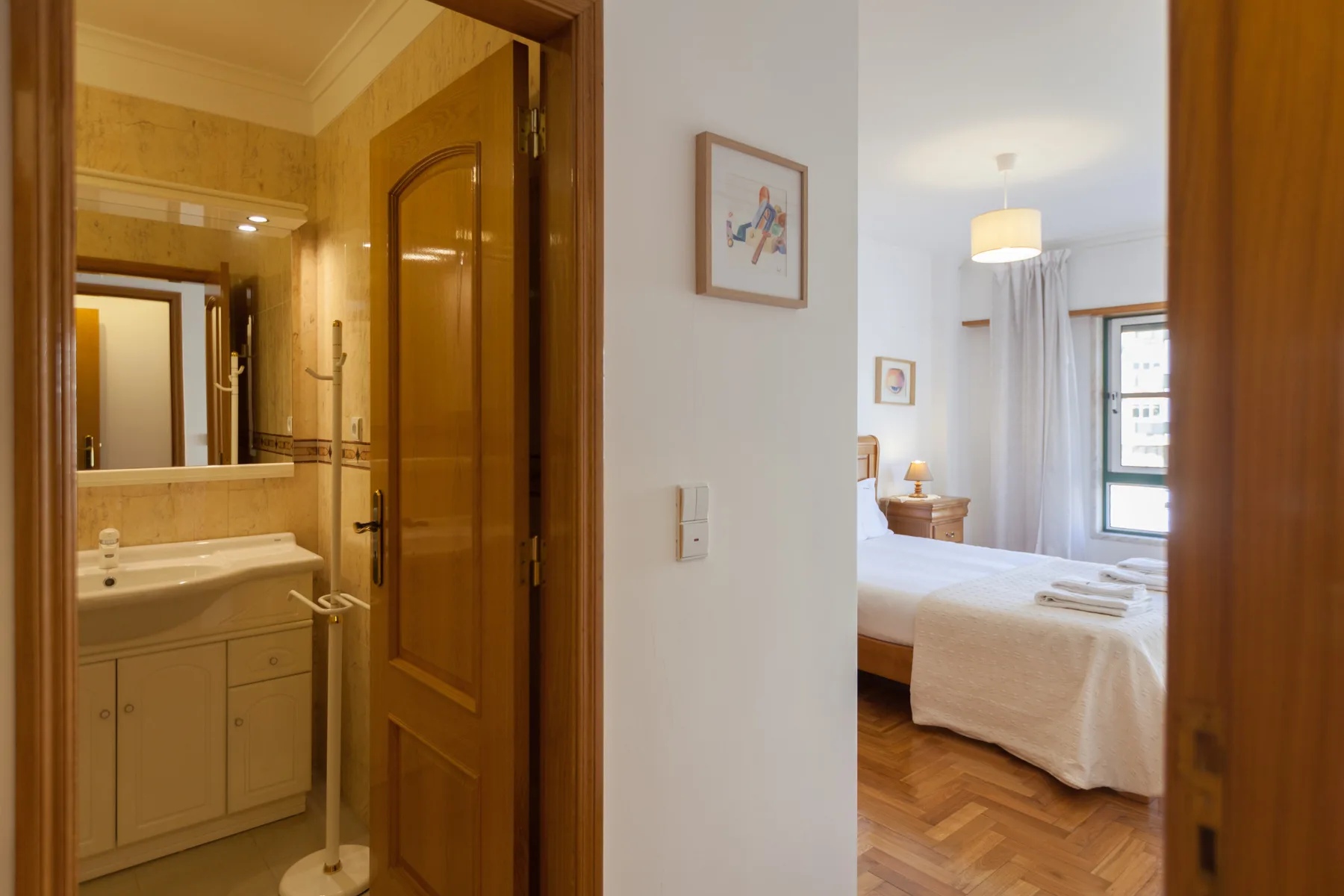 Se ve un dormitorio con la cama arreglada a través de una puerta abierta, junto a un baño.