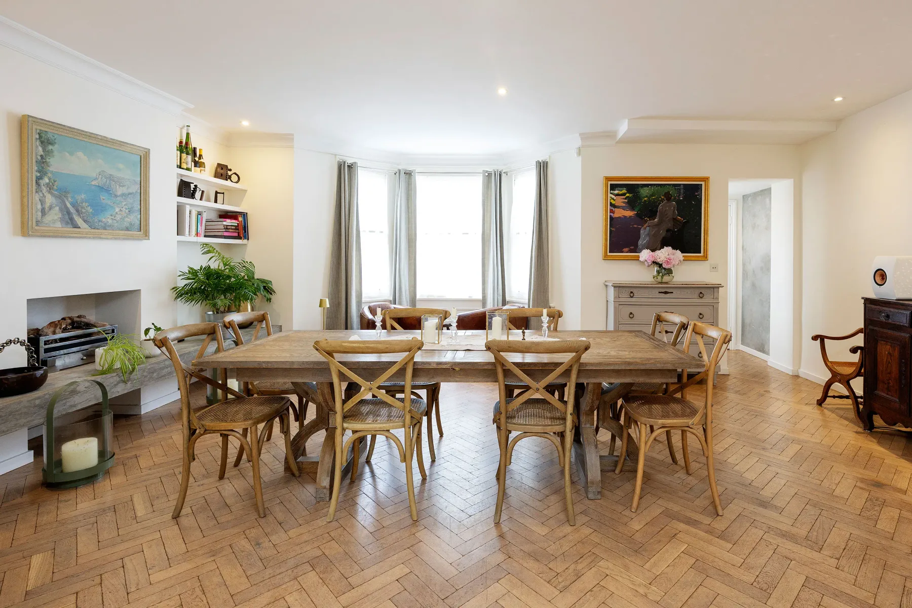 Un comedor con una larga mesa de madera y sillas frente a ventanas altas.