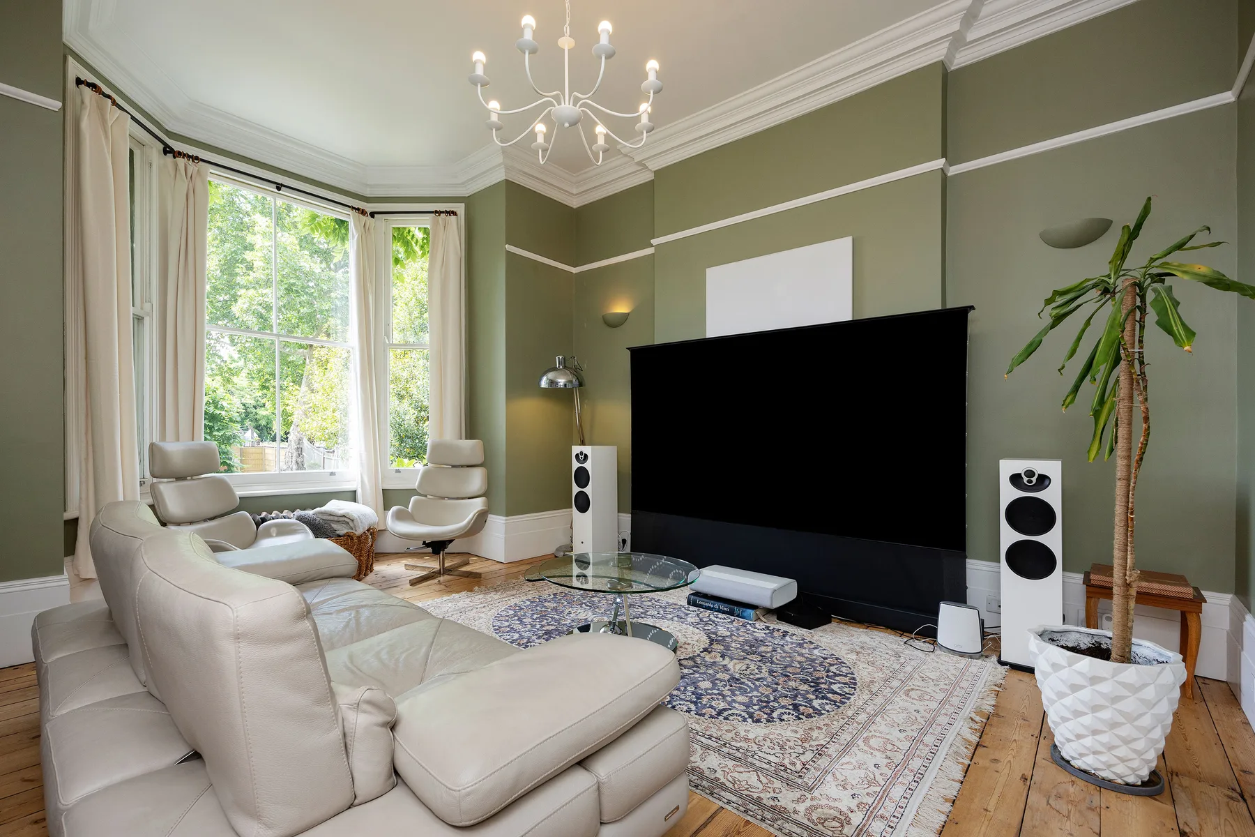 A living room with light seating, a large television, and tall windows.