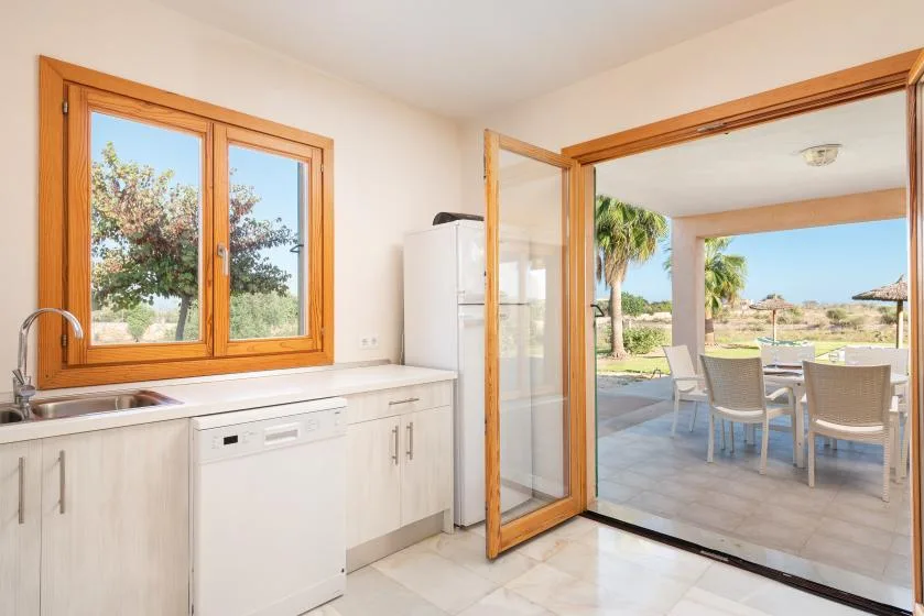 Una cocina luminosa se abre a una zona de comedor exterior mediante puertas de vidrio.