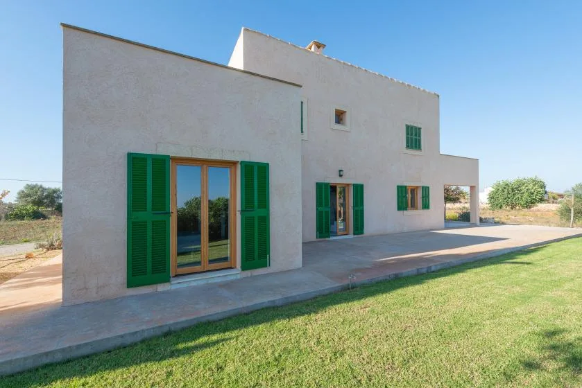 Una casa blanca con contraventanas verdes se encuentra junto a un césped bajo un cielo despejado.