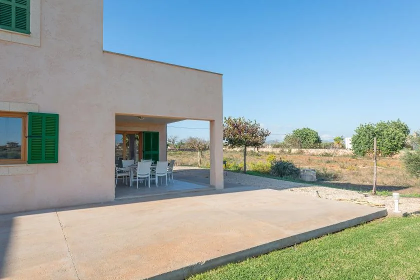 Un patio de una casa con asientos al aire libre junto a un jardín con césped.