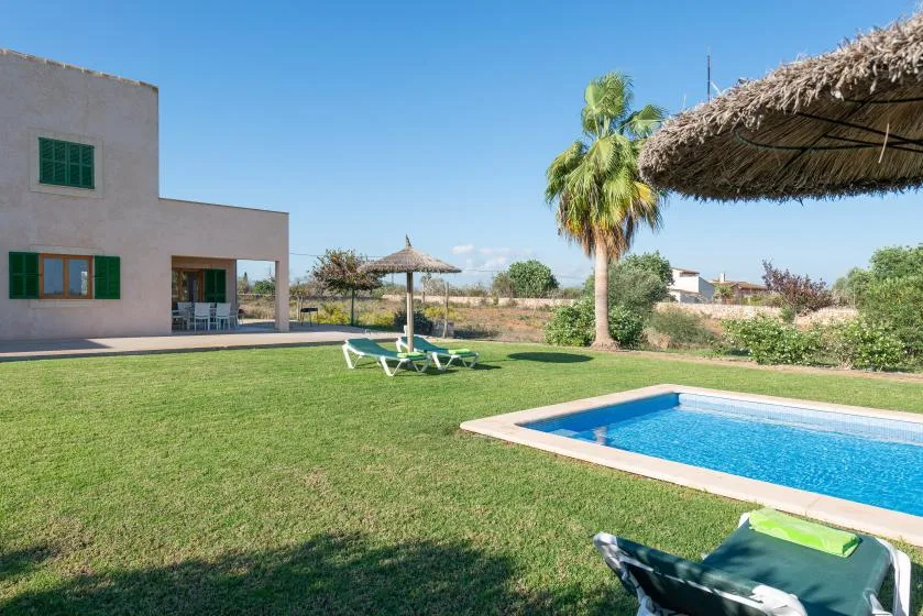 Una piscina y un césped verde están junto a una casa moderna bajo un cielo despejado.