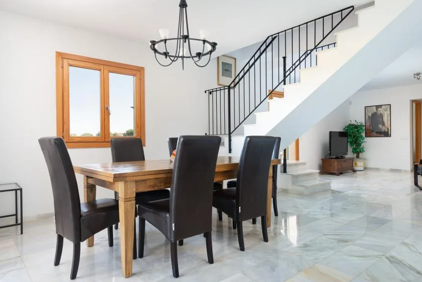 Comedor con una mesa de madera y asientos oscuros bajo una escalera.