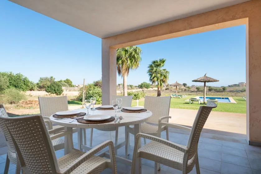 Una zona de comedor en un patio cubierto da a un césped y una piscina.