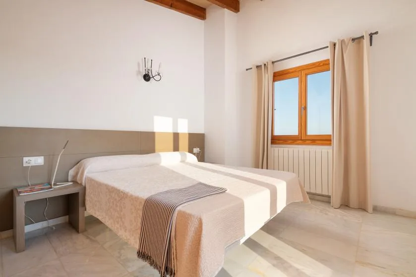 Un dormitorio con una cama bien hecha junto a una ventana con cortinas.