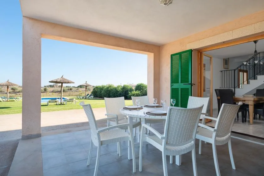 Una zona de comedor en un patio cubierto da a un jardín, con una mesa y sillas.