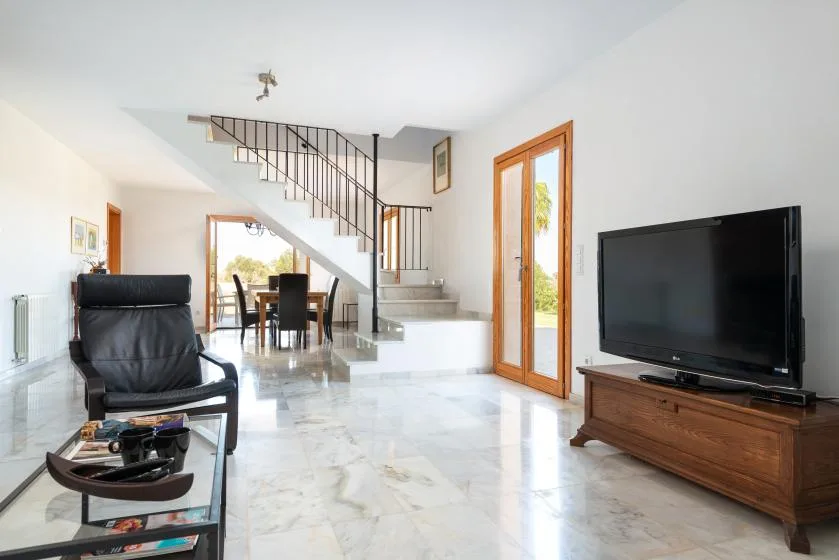 Una sala luminosa con asientos, un televisor y una escalera.