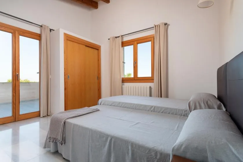 Un dormitorio luminoso con camas junto a ventanas altas y una puerta de madera.