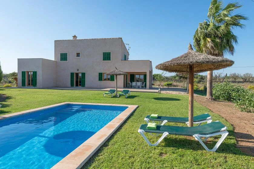 Una casa moderna se alza detrás de una piscina y un césped.