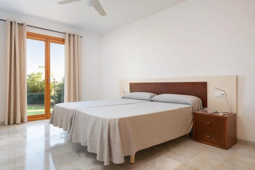 Un dormitorio luminoso con una cama tendida y puertas de vidrio que dan a la vegetación.