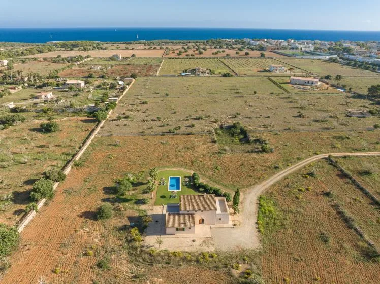 Vista aérea de una casa pequeña y una piscina entre campos abiertos cerca de la costa.