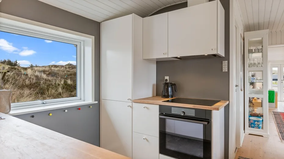 Una cocina compacta con gabinetes blancos y una encimera de madera junto a una ventana grande.