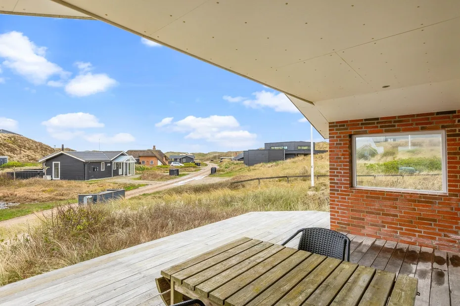 Una terraza de madera con una mesa da a un terreno cubierto de hierba y casas cercanas.