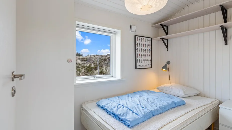 Un dormitorio pequeño con una cama bajo estantes abiertos y una ventana.