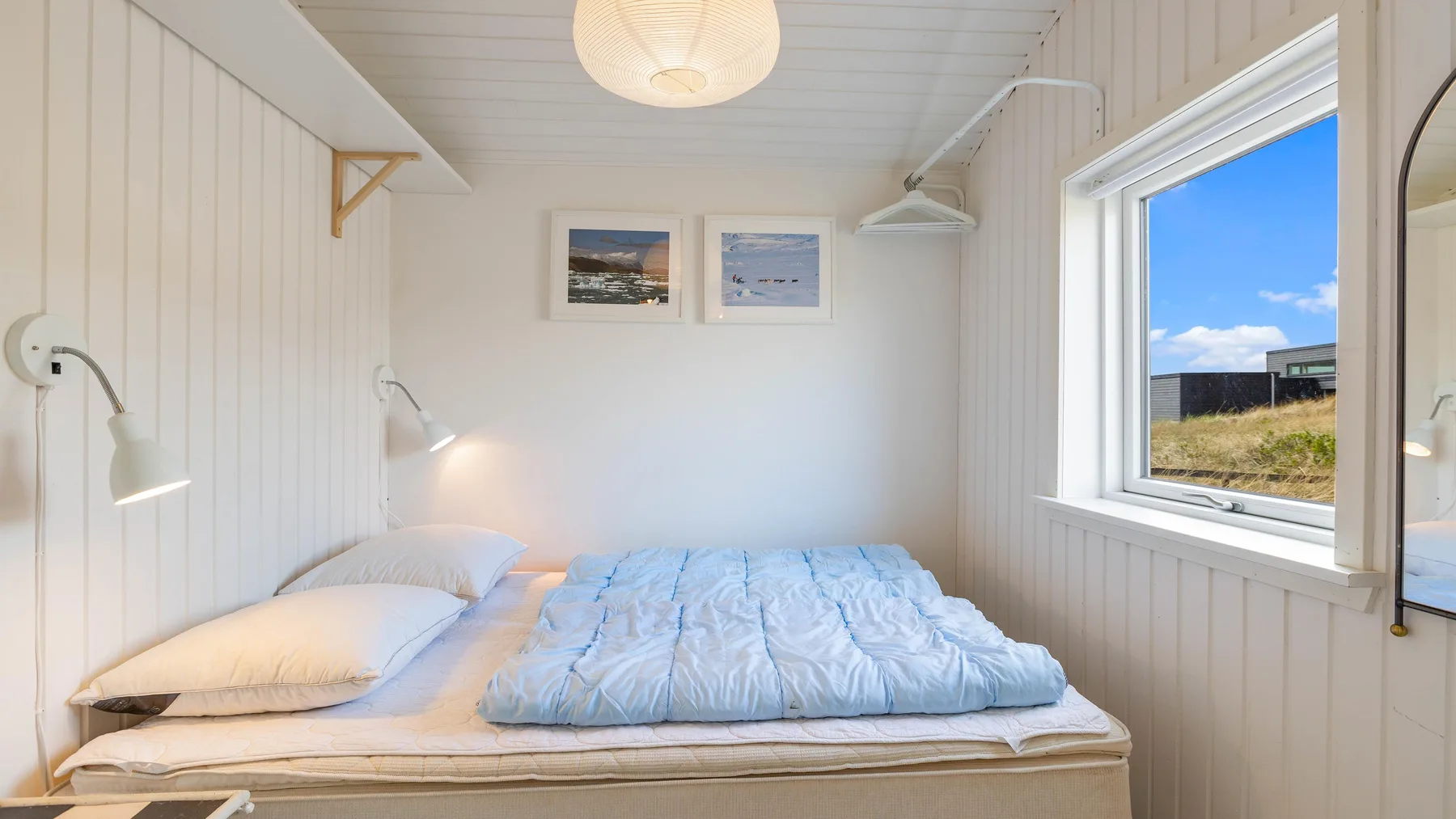 Un dormitorio con una cama bajo dos cuadros y una ventana grande.