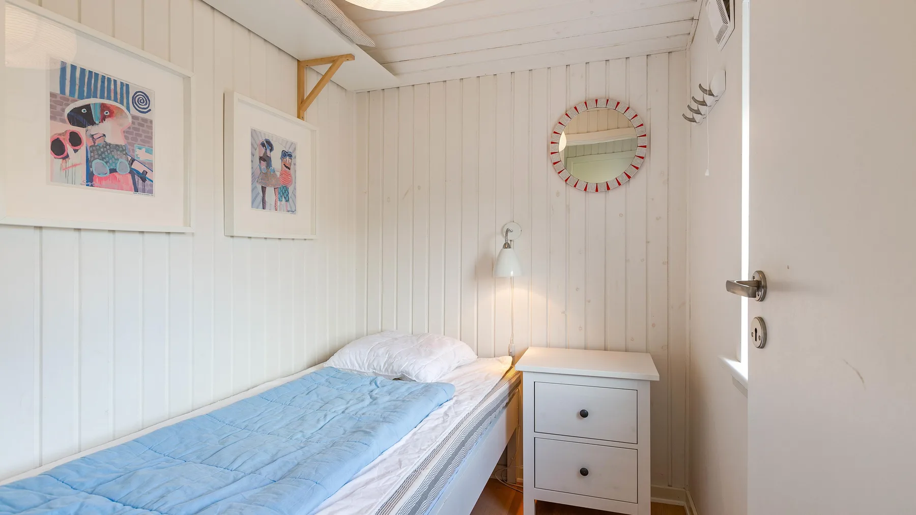 Un dormitorio pequeño con una cama individual, una mesita de noche y cuadros enmarcados.