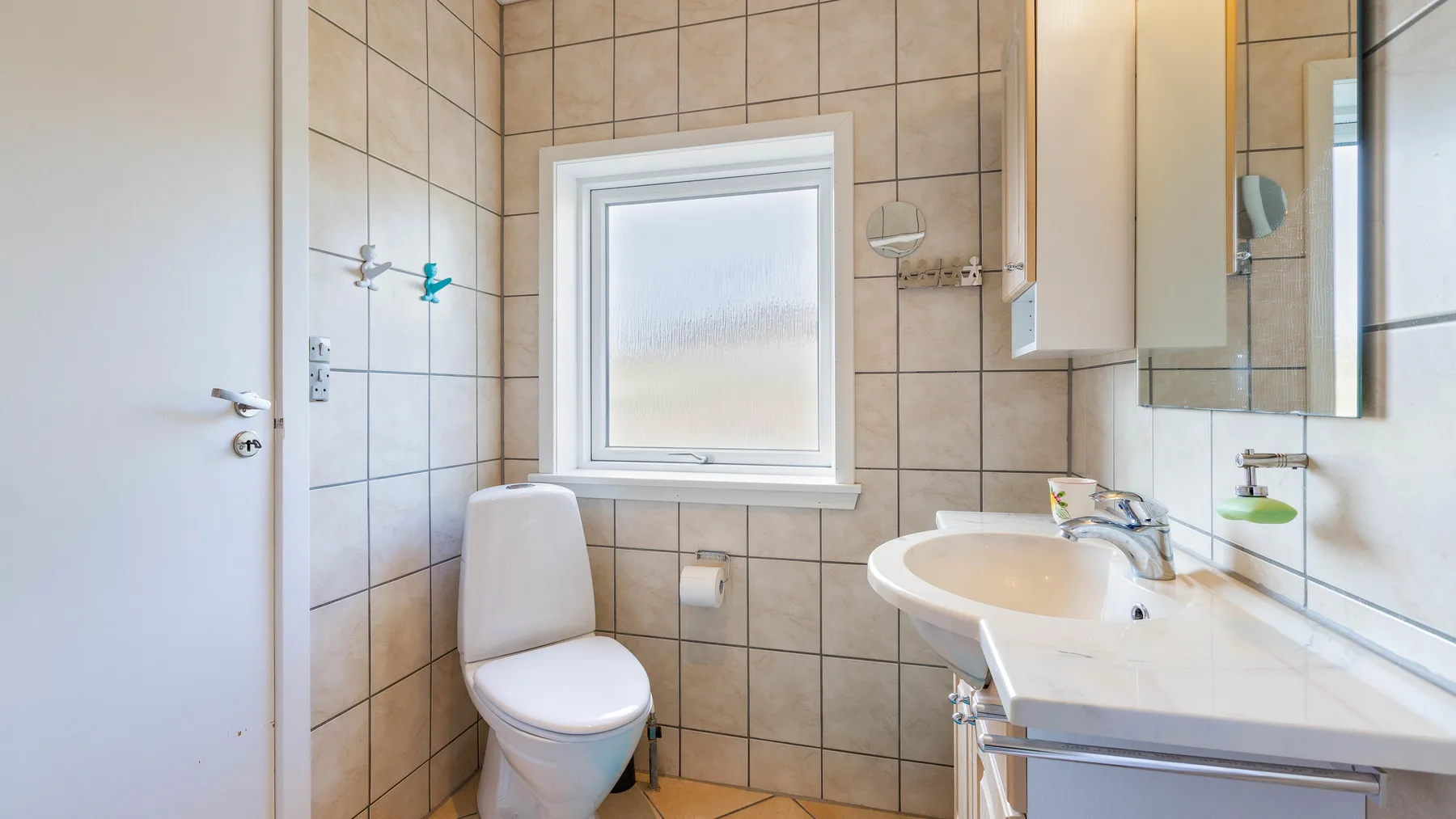 Un baño con azulejos, inodoro, ventana y lavabo.