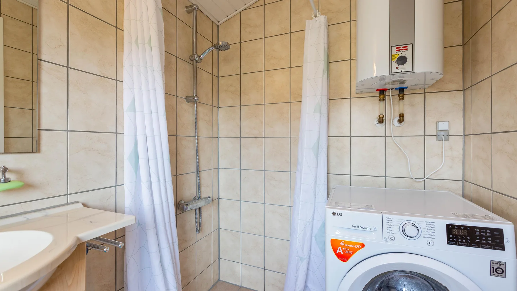 Un baño alicatado con una lavadora y cortinas de ducha.