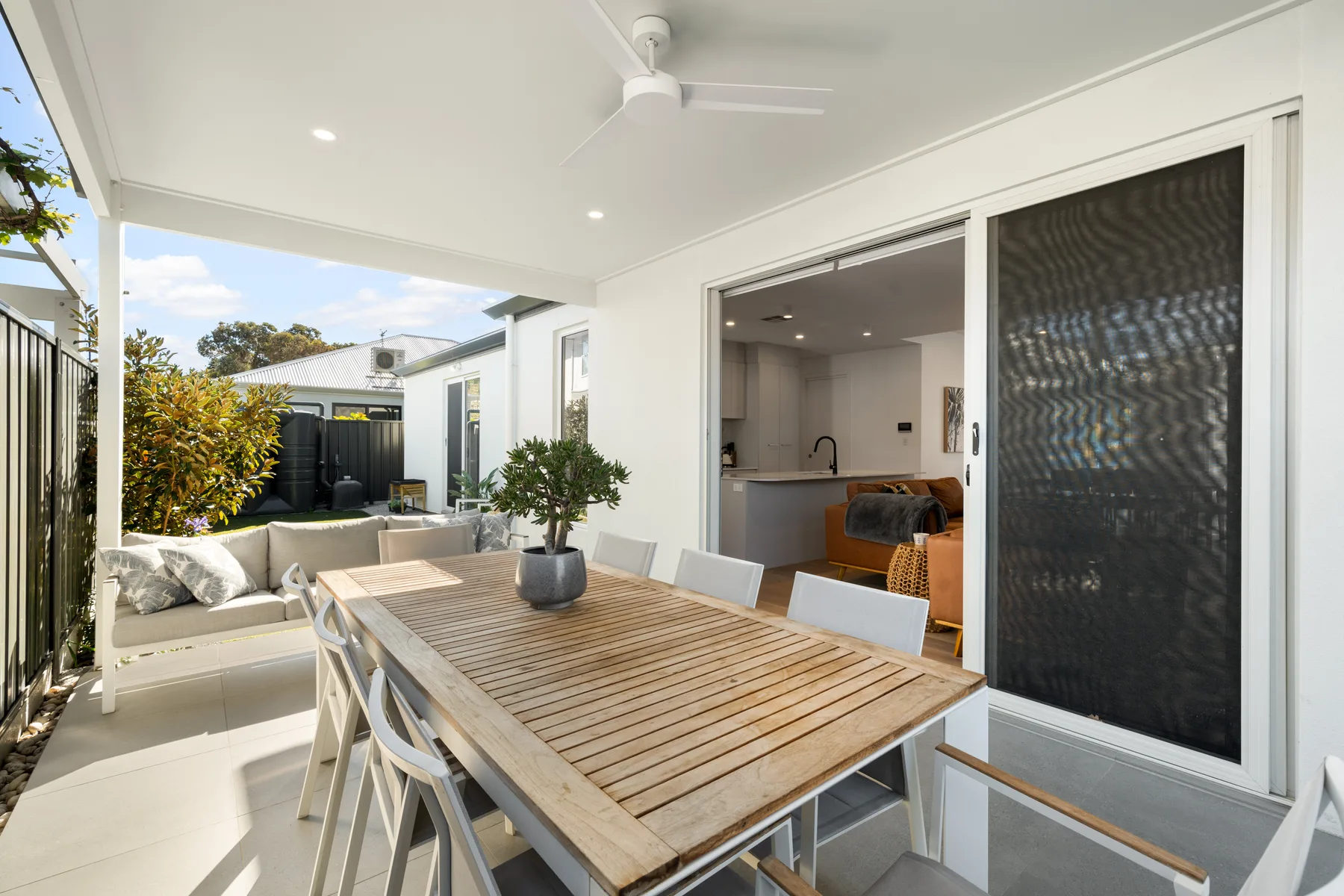 Disfruta de comidas al aire libre bajo el patio cubierto, donde una amplia mesa de comedor, asientos acolchados y un ventilador de techo crean un ambiente exterior acogedor.