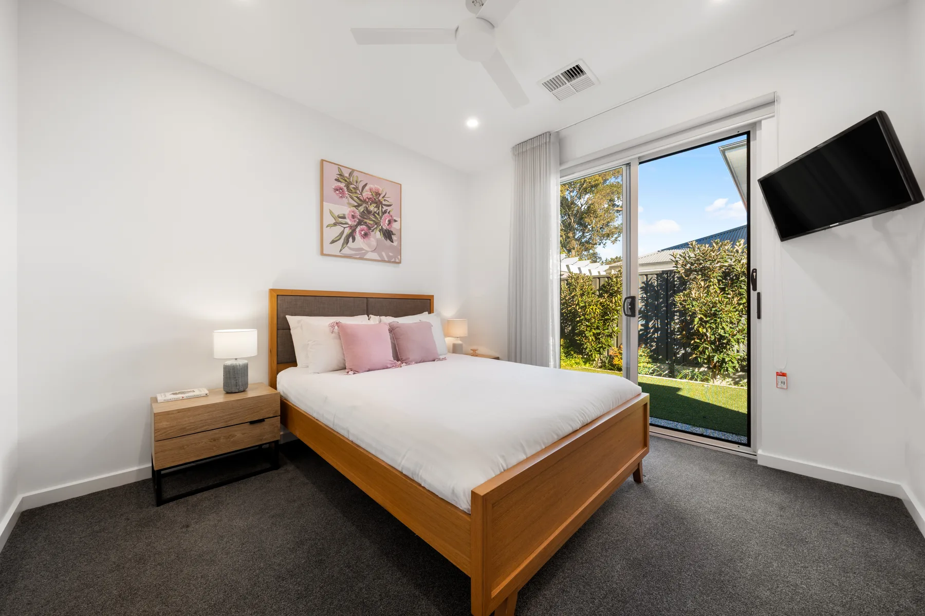 Un dormitorio luminoso con una cama junto a puertas de vidrio que dan a un jardín.