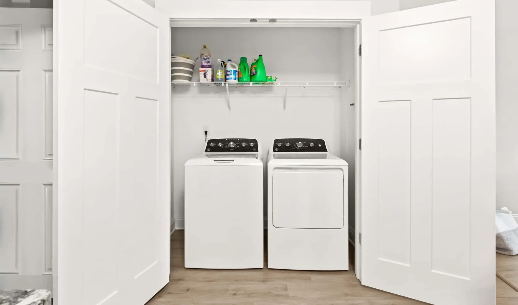 A laundry area with a washer and dryer beneath a shelf of cleaning supplies.