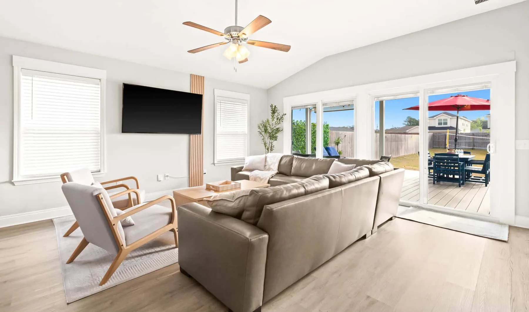 A bright living room with seating facing a television and windows overlooking a patio.
