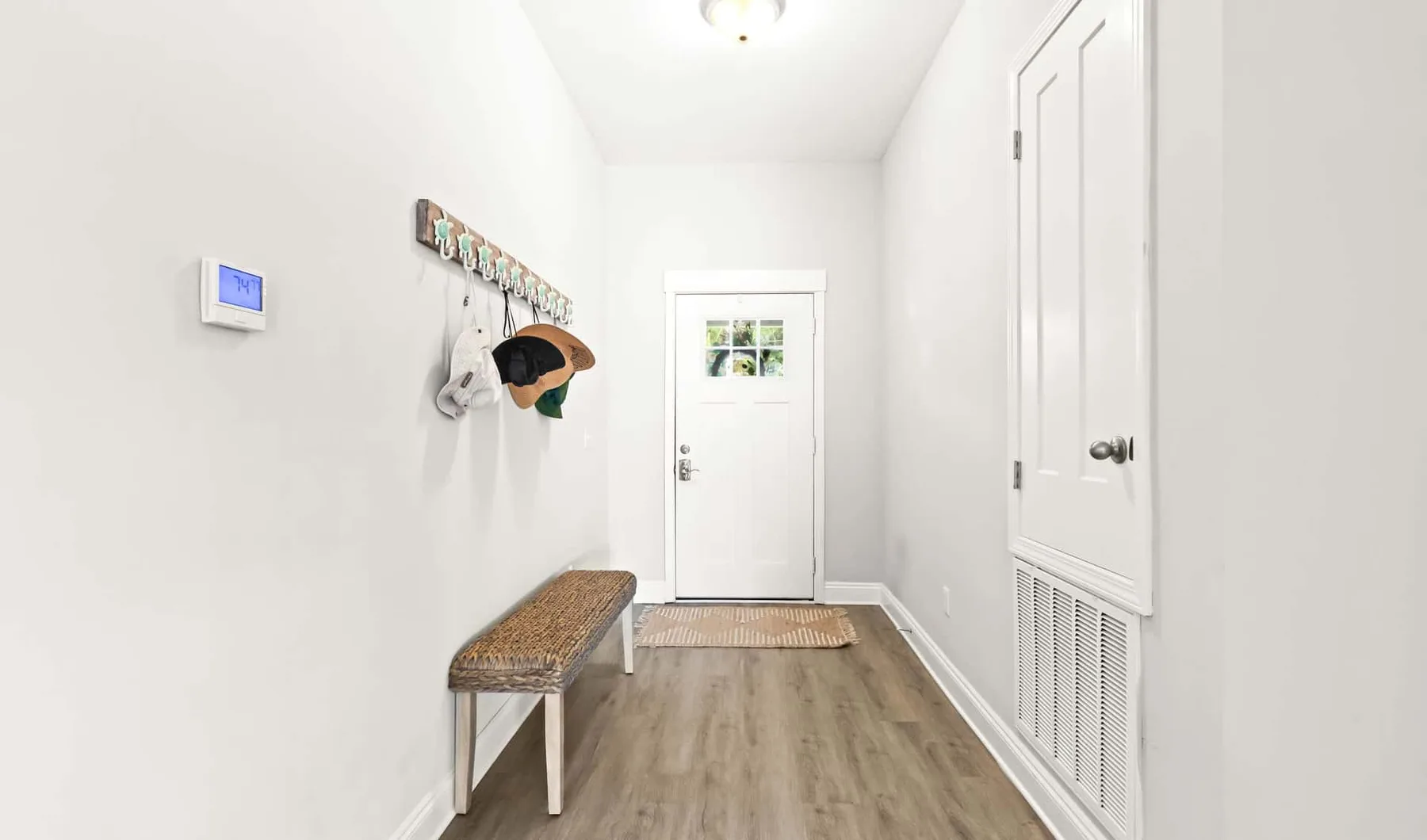 A bright entry hallway with a bench, wall hooks, and a door at the far end.