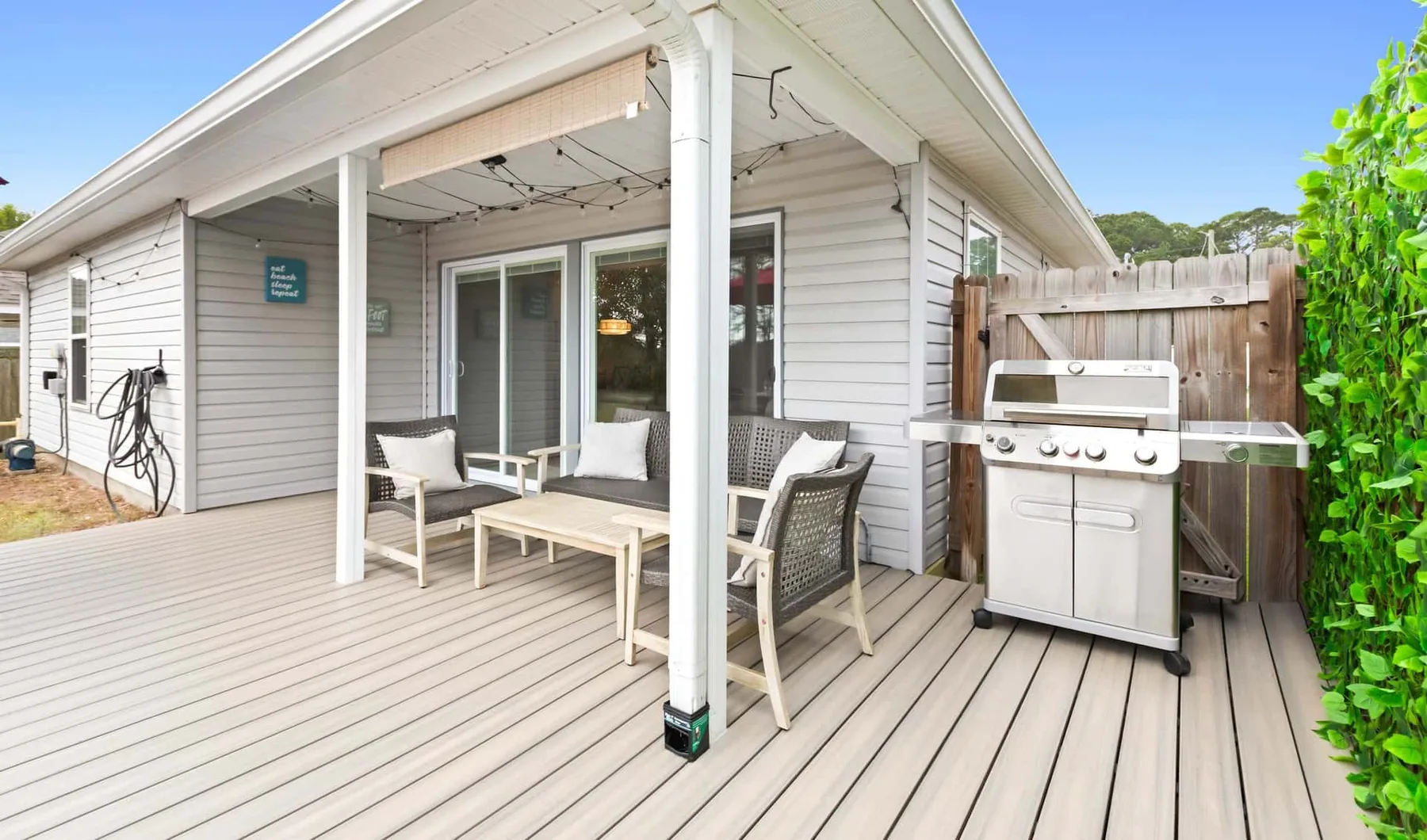 A covered outdoor deck has seating beside a barbecue grill.