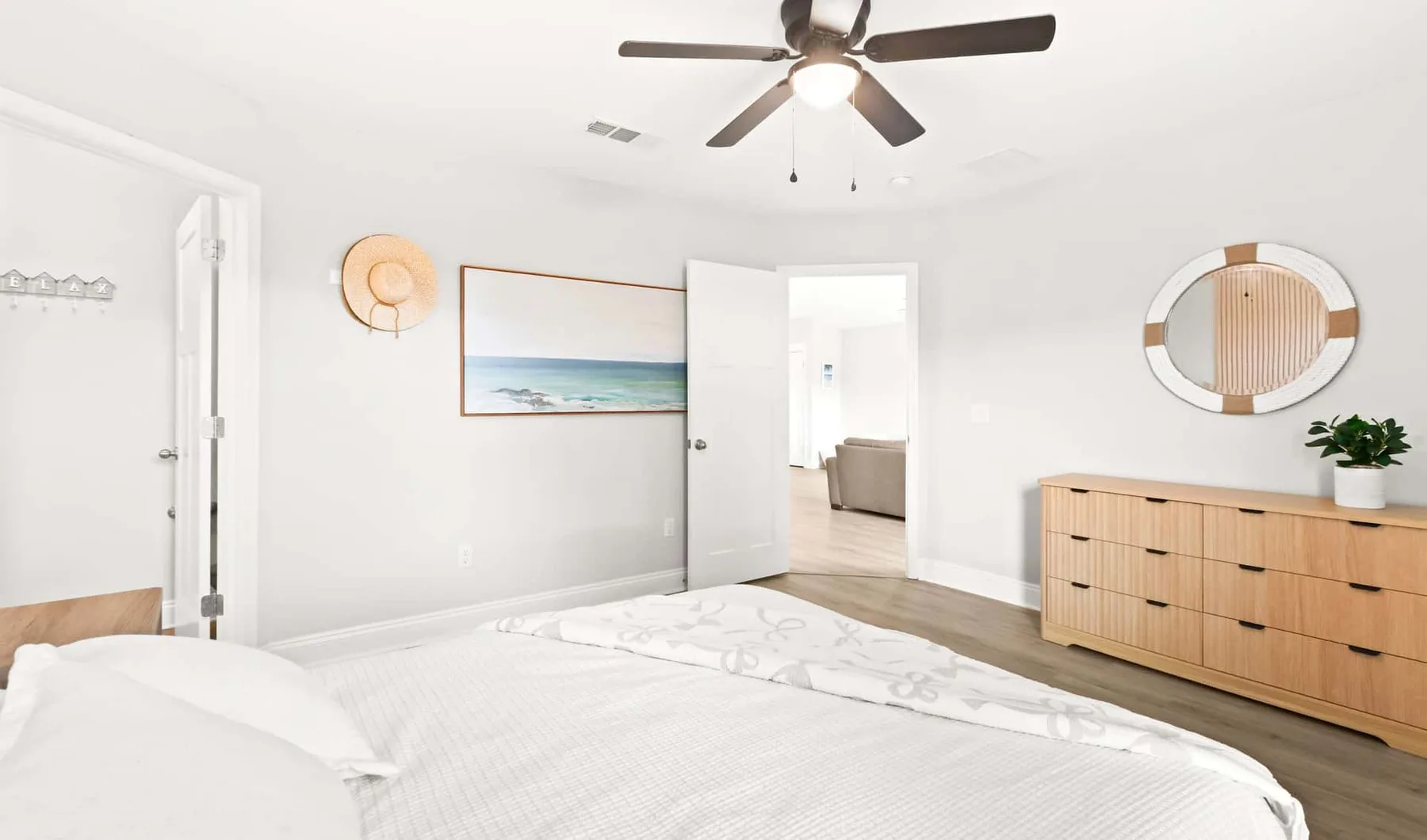 A bright bedroom with a bed, ceiling fan, and wooden dresser.