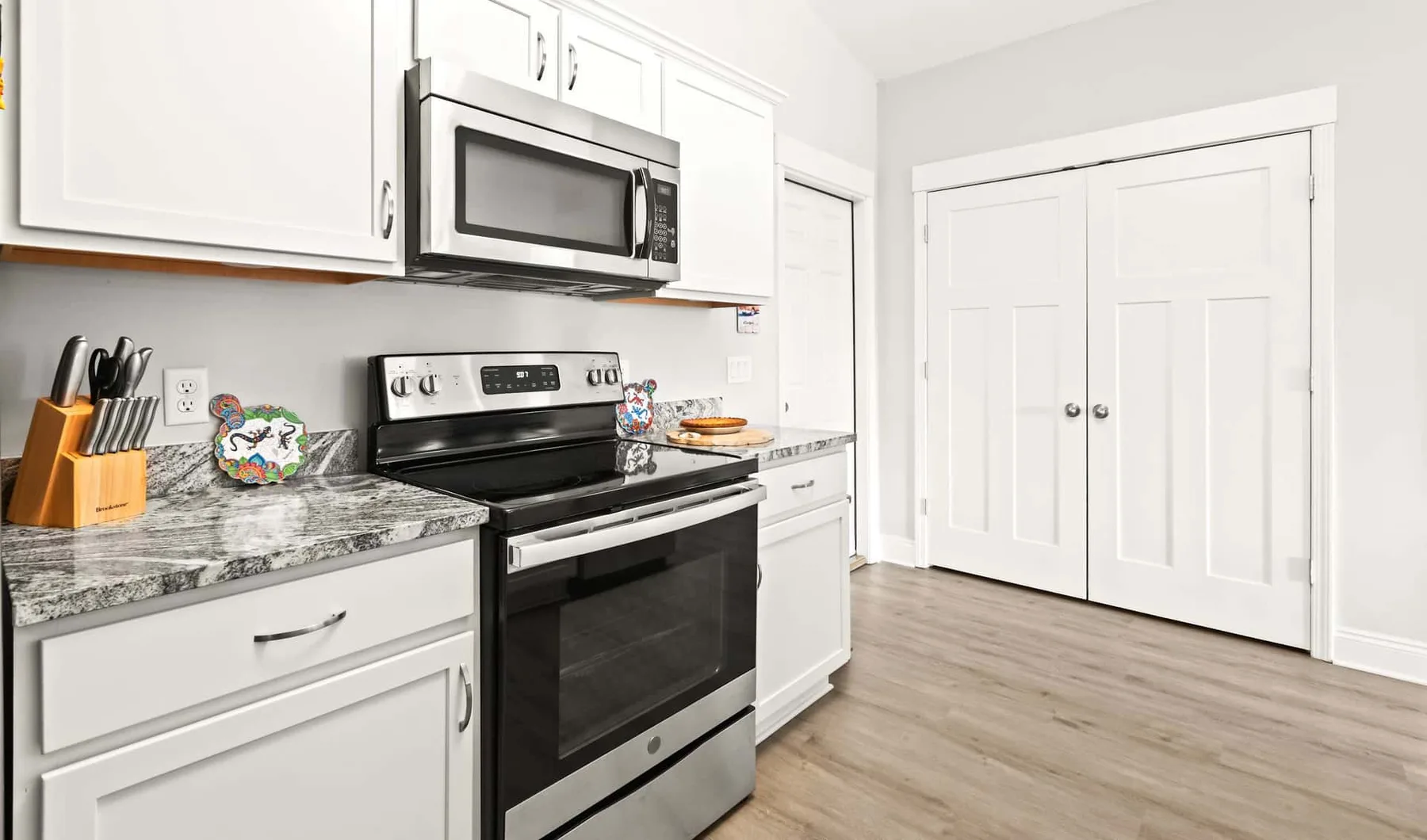 A bright kitchen with white cabinets, a stove, and a microwave.