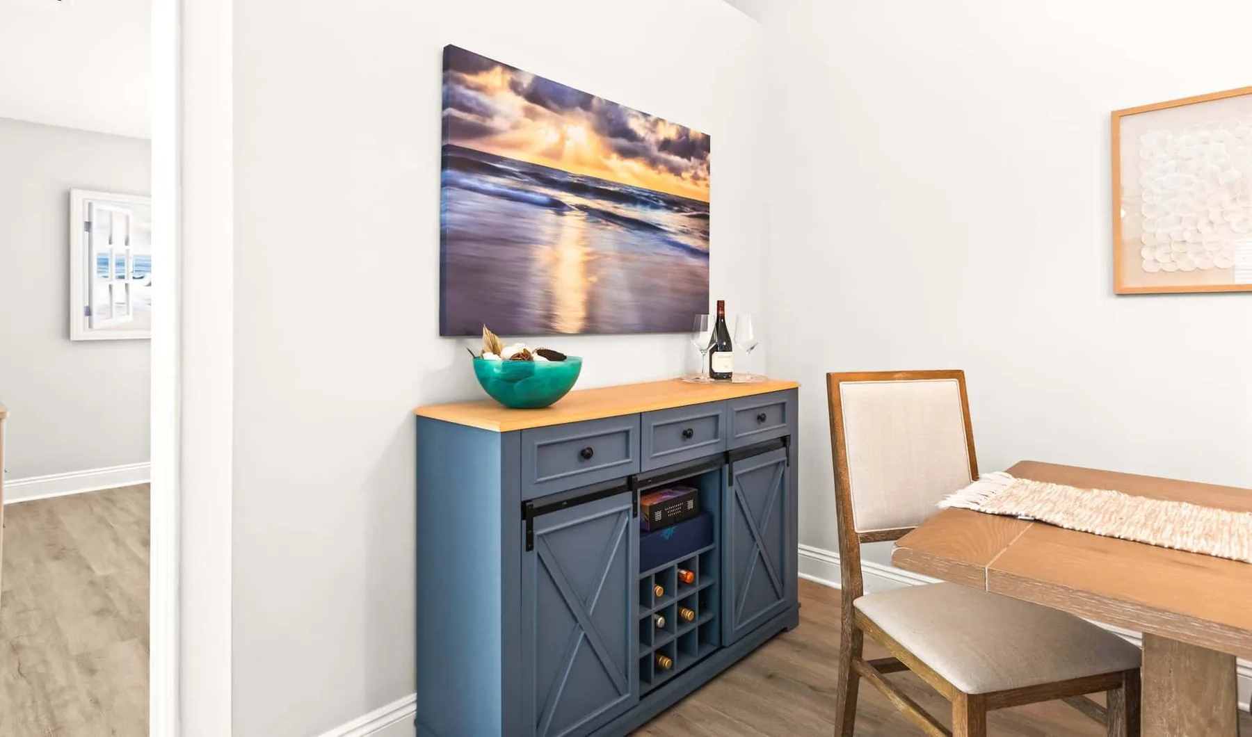 A dining area features a blue sideboard beneath a large beach photograph.