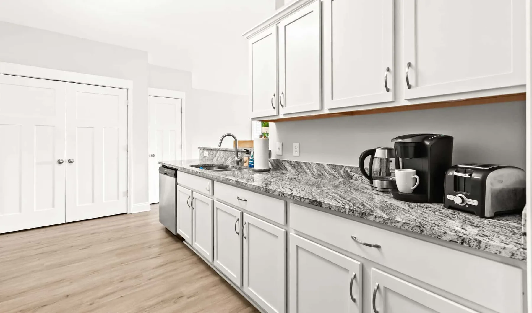 A bright kitchen with white cabinets and a countertop coffee maker.