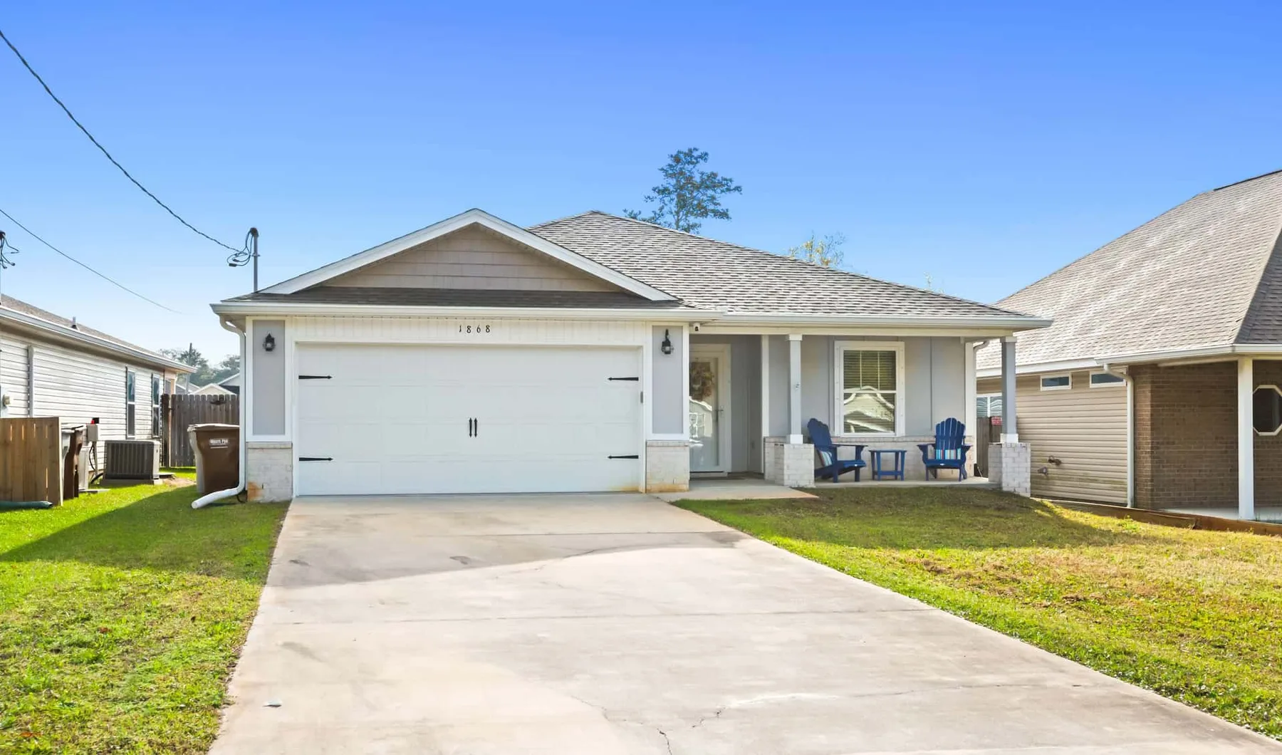 A single-story house with a wide driveway and two chairs on the porch.