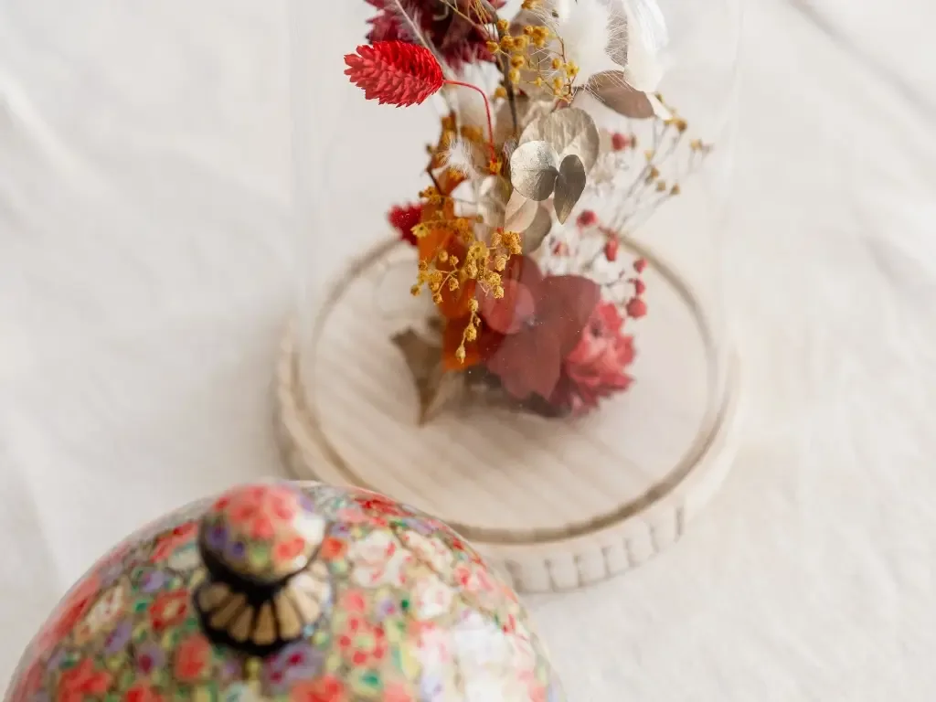 Un arreglo floral en un jarrón de vidrio está junto a un objeto colorido con estampado.