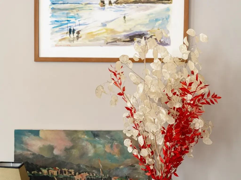 Cuadros en la pared y un arreglo decorativo de ramas rojas y blancas en una habitación.