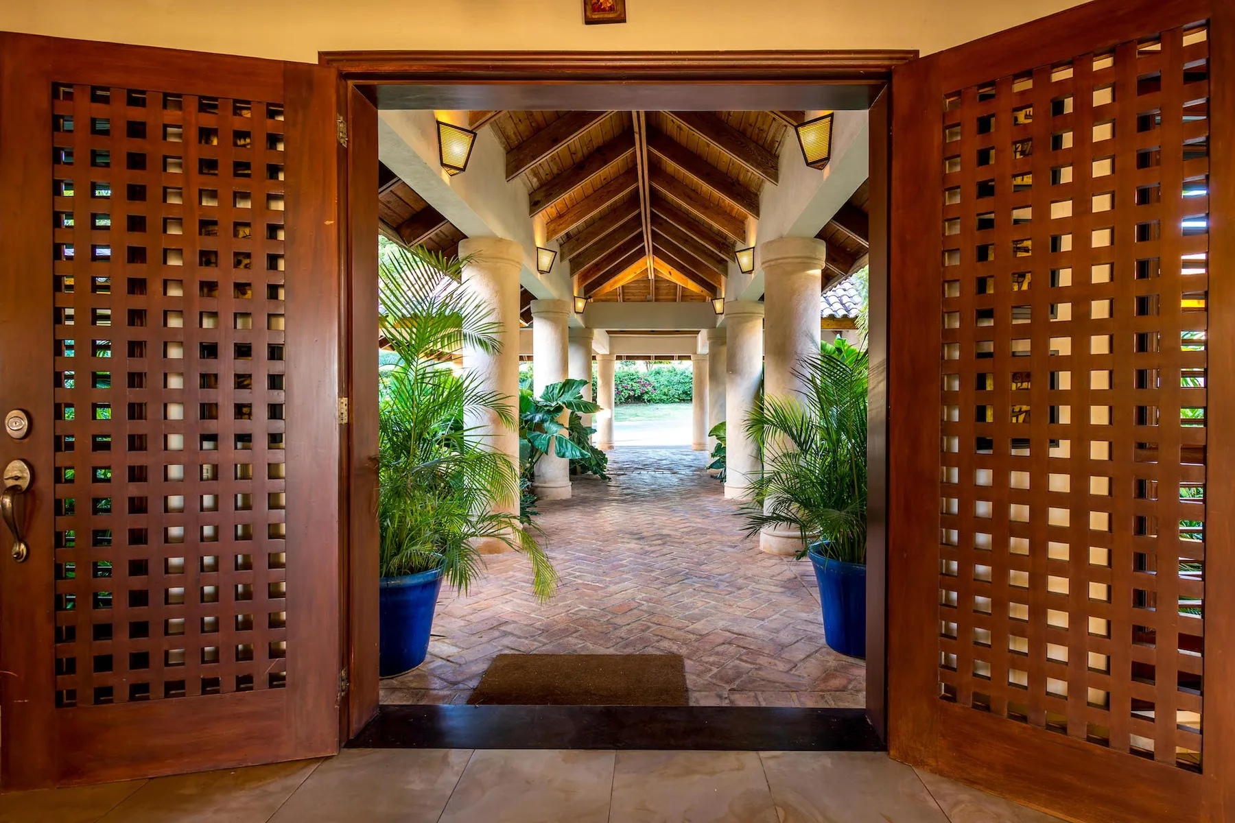 A covered passage framed by wooden lattice doors, with potted plants along the walkway.