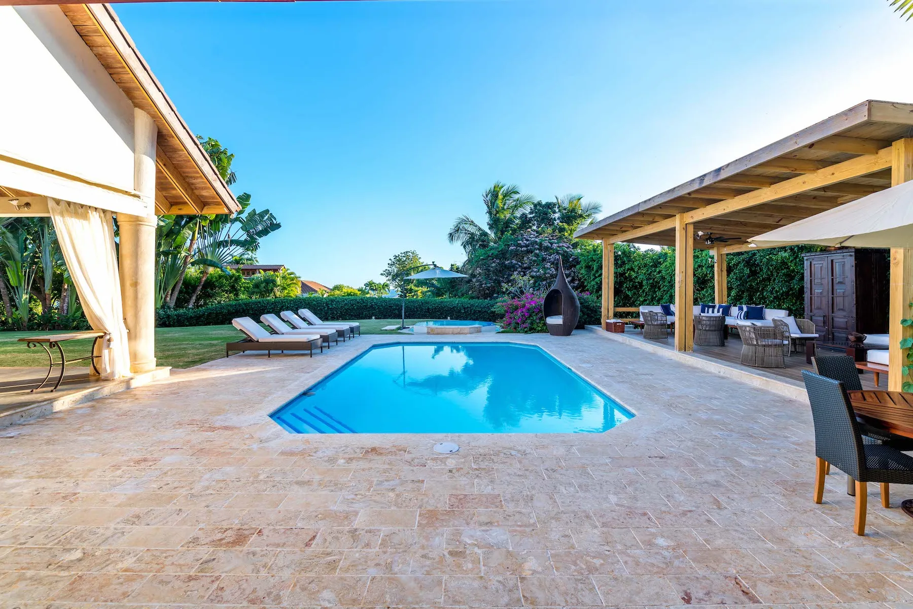 Una piscina al aire libre está en un patio pavimentado junto a una zona de estar cubierta.