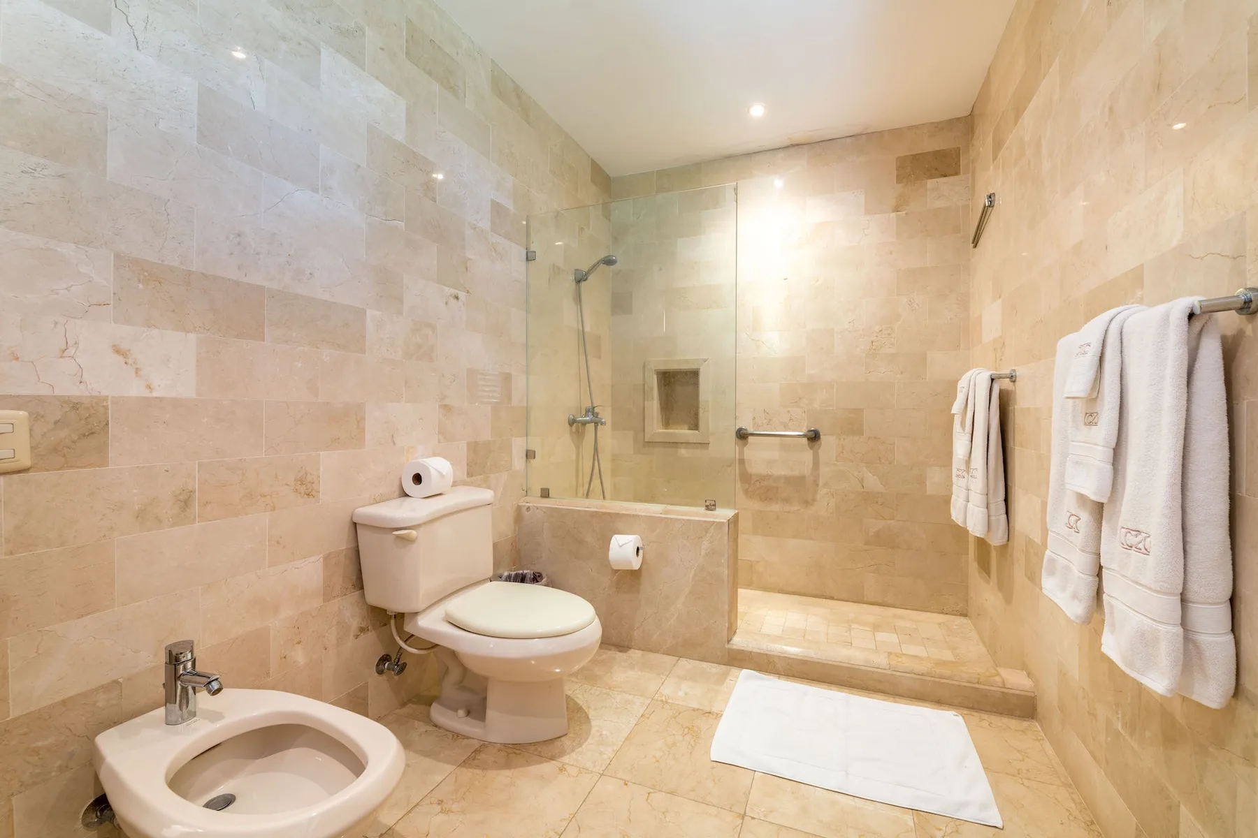 Un baño alicatado con ducha, inodoro y toallas colgadas en la pared.